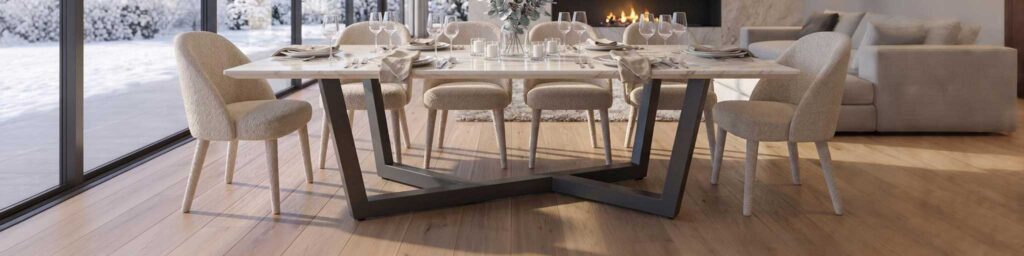 Moderne eetkamer met een witte tafel gedekt voor zes personen, beige gestoffeerde stoelen en een open haard; grote ramen bieden uitzicht op de besneeuwde buitenlucht.