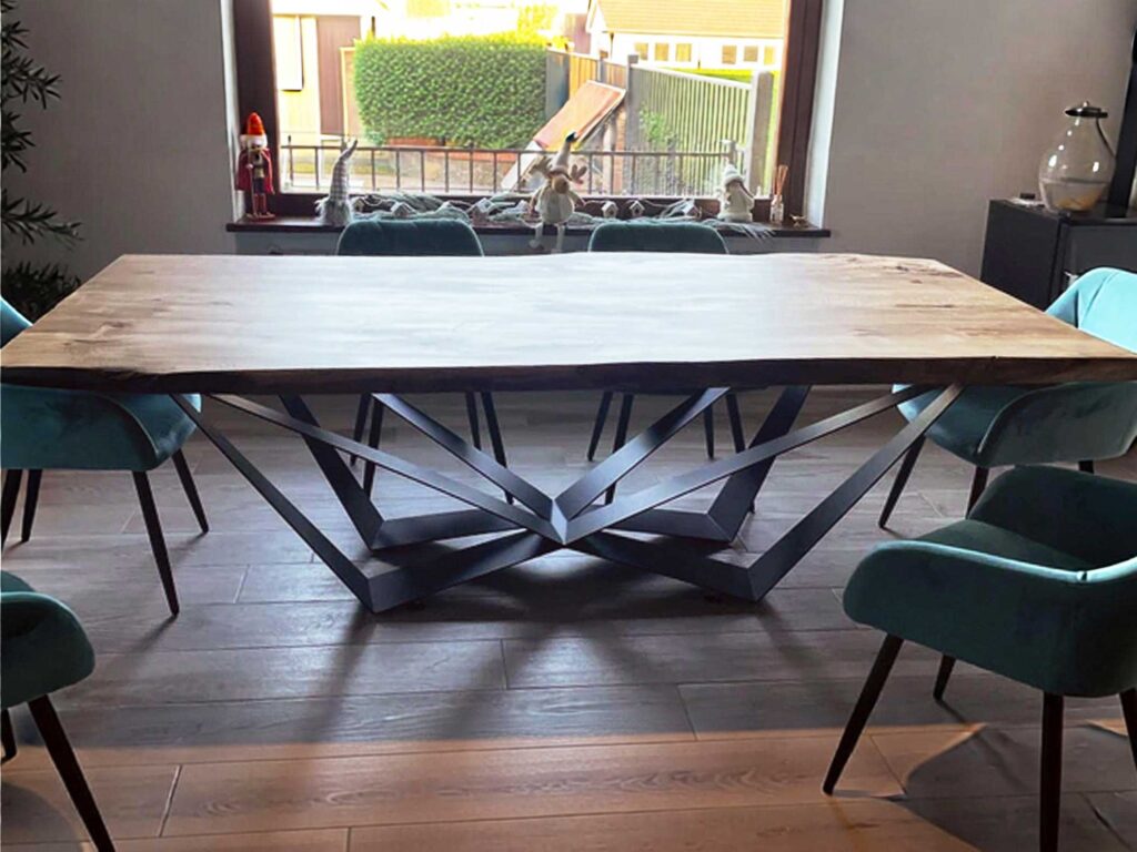 Large wooden dining table with teal chairs and a geometric metal base, in a bright dining room overlooking a backyard through a window with small gnome figurines on the sill.