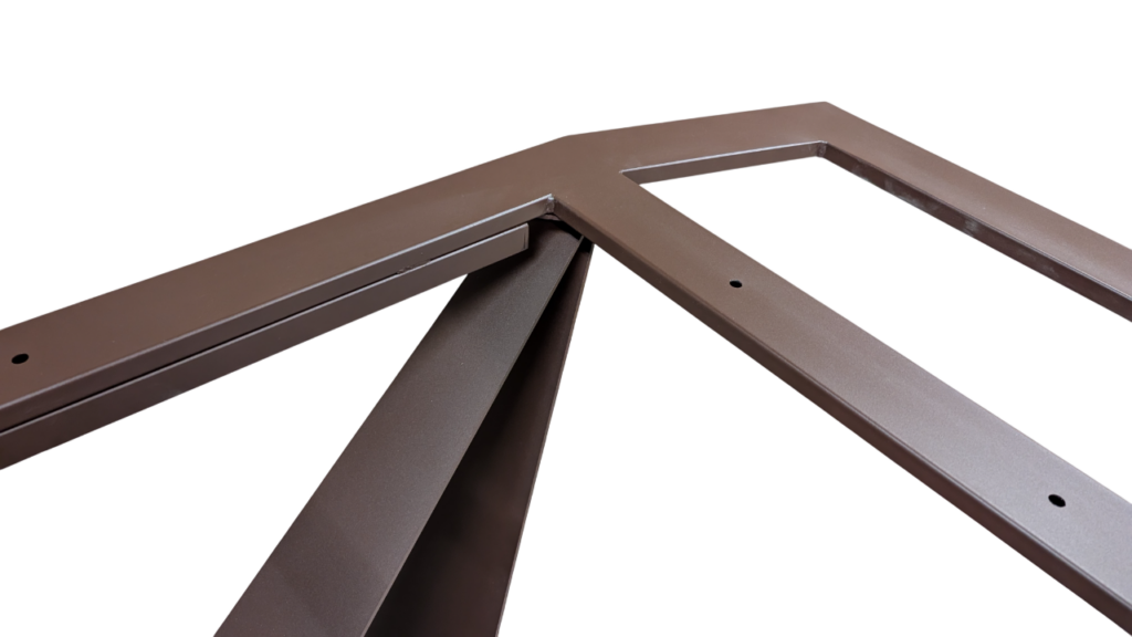 Close-up of a brown metal frame joint where two rails meet at a corner, with visible holes for fasteners and a reinforcing brace nearby.